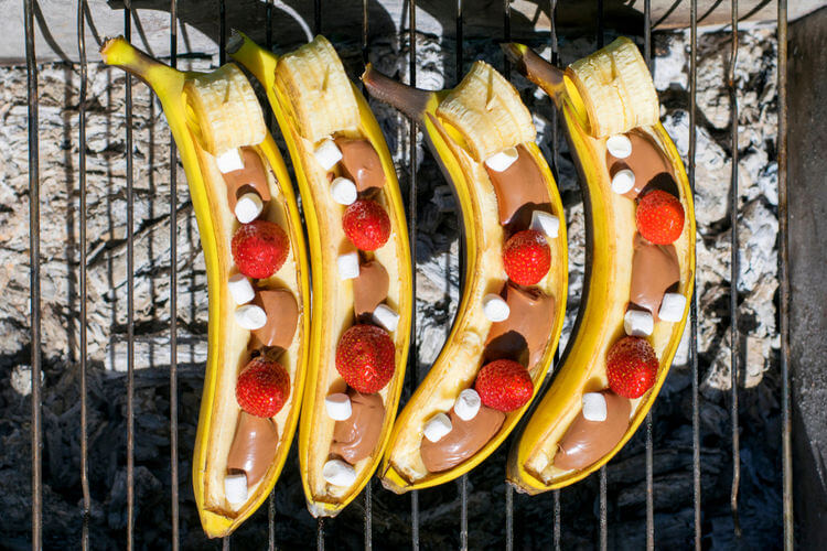 Banana boats cooking on a grill with chocolate and marshmallow