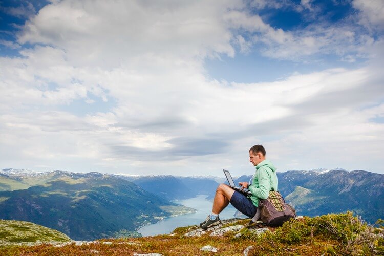 Man sitting on rock overlooking lake on laptop