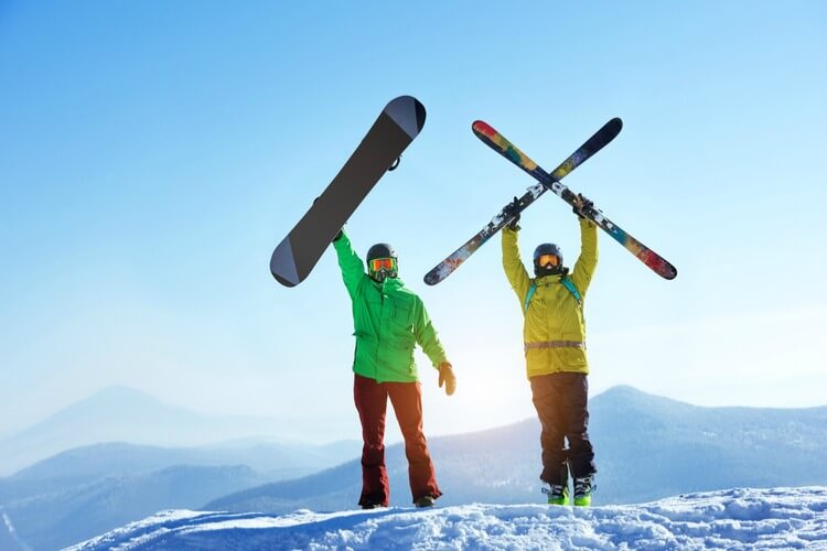Snowboarder and skier standing on mountain holding boards above their heads