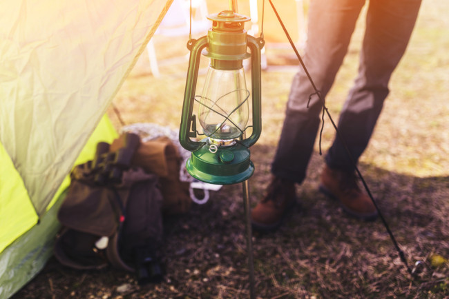 Woman camping standing next to lantern and tent
