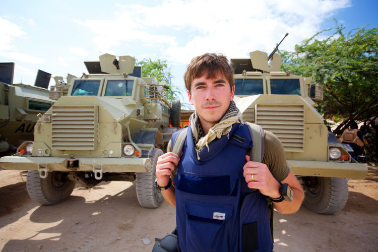 Adventurer Simon Reeve stood in front of military trucks