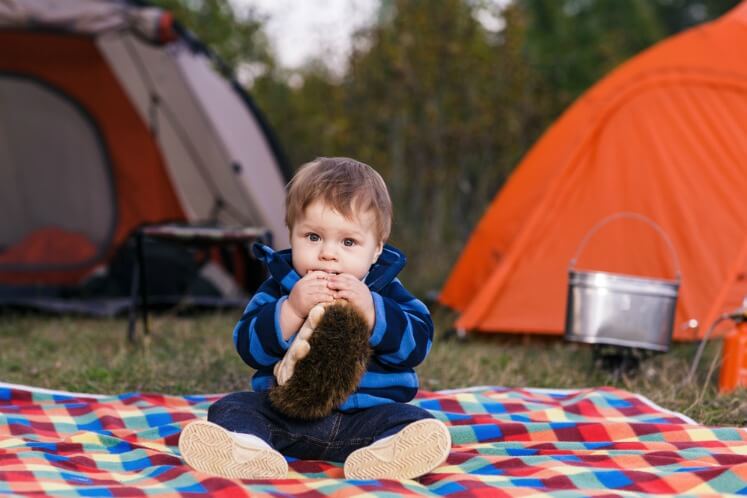 Baby camping sitting on a picnic rug